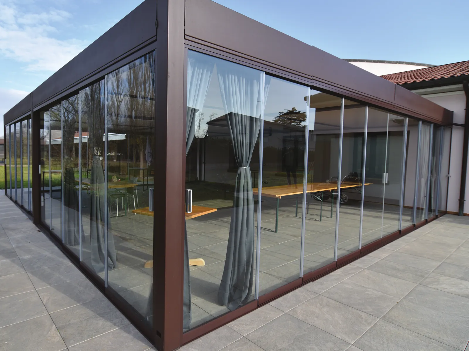 Sliding Floor con profili marrone che chiude su tre lati un portico su pavimento in pietra